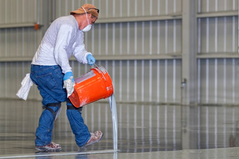 worker pouring self levelling epoxy mixture on the floor